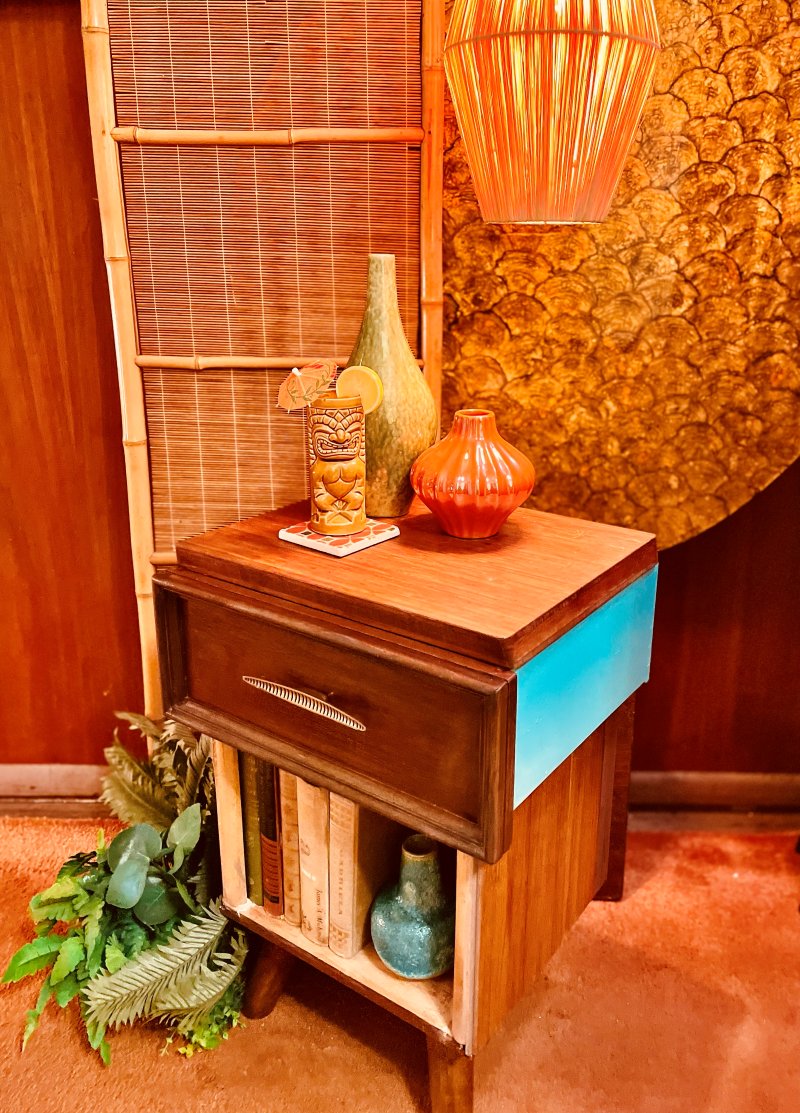 Freestanding nightstand by Jason, a single drawer over an open shelf with one side painted teal, styled in a tiki vignette
