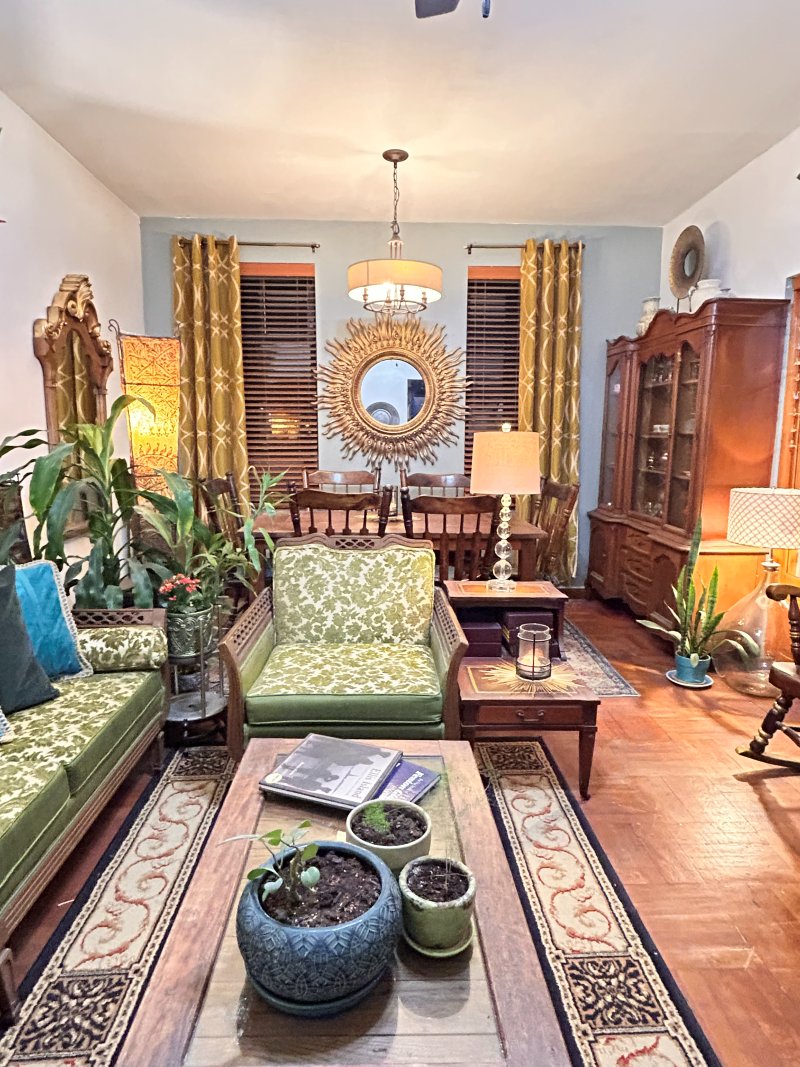 Living and dining room with green damask seating and a gilt sunburst mirror